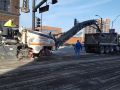 big asphalt machine pouring dug up road into a dumpster truck