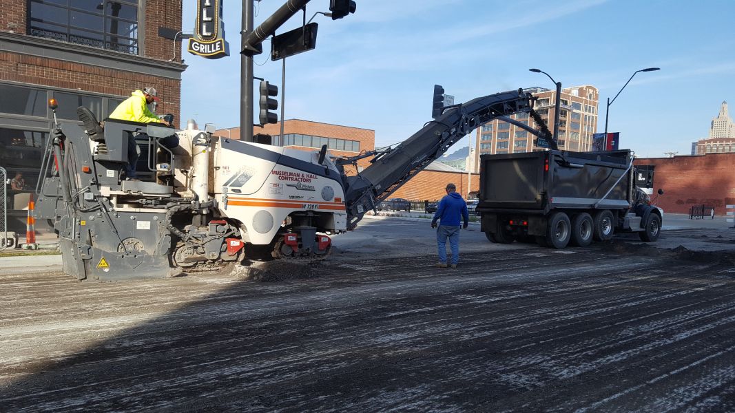 big asphalt machine pouring dug up road into a dumpster truck